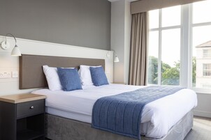 A modern hotel room with a large bed, a nightstand, a desk, and a window with curtains.