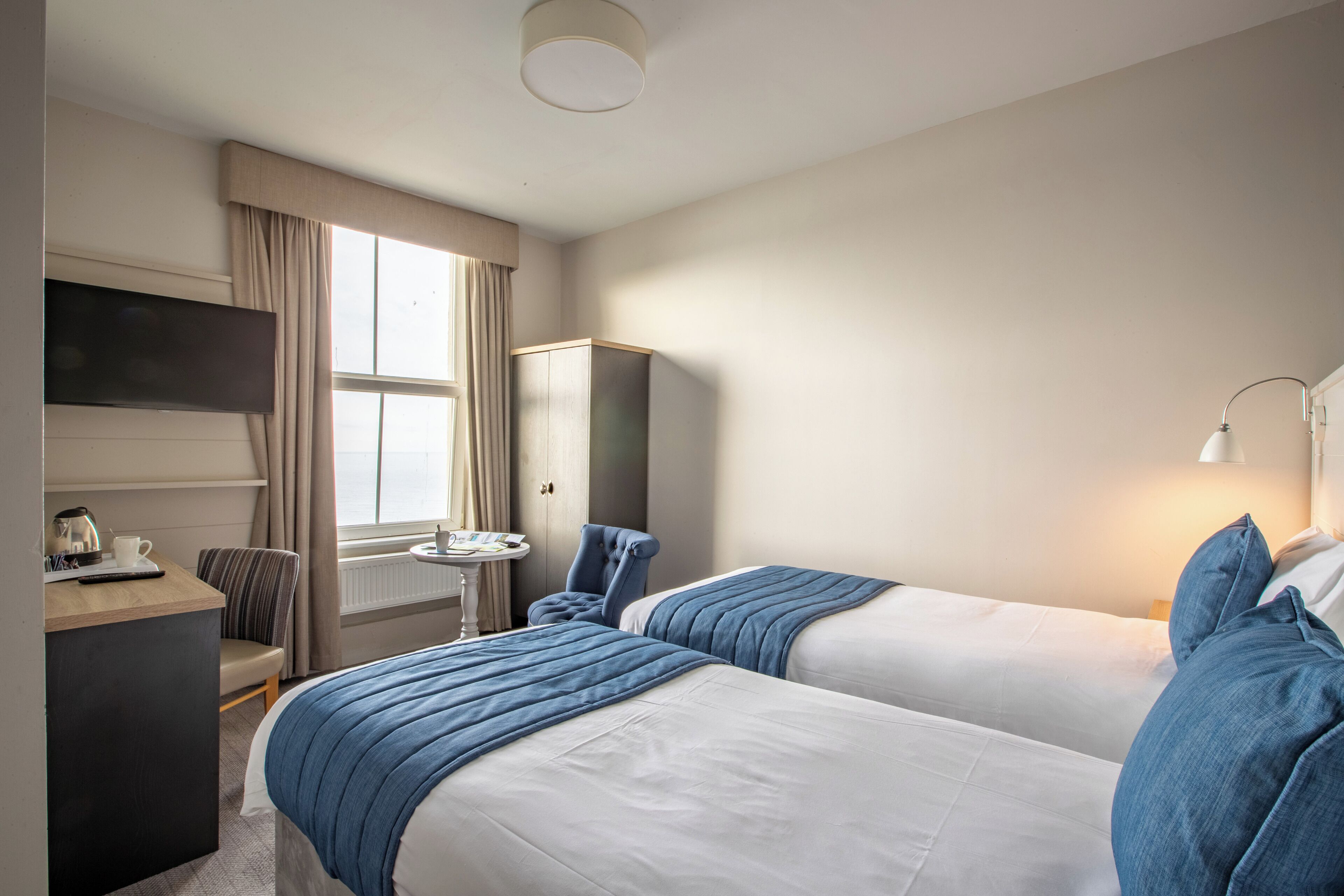 Una habitación de hotel con dos camas, un escritorio, una silla, un televisor y una lámpara.