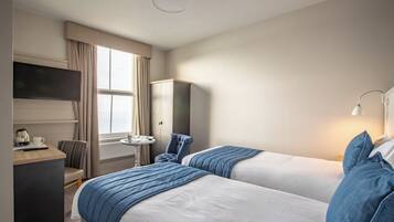 A hotel room with two beds, a desk, a chair, a TV, and a lamp.