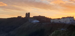 Un castillo histórico con una torre destacada, ubicado en una colina con vistas a un pueblo de arquitectura tradicional.