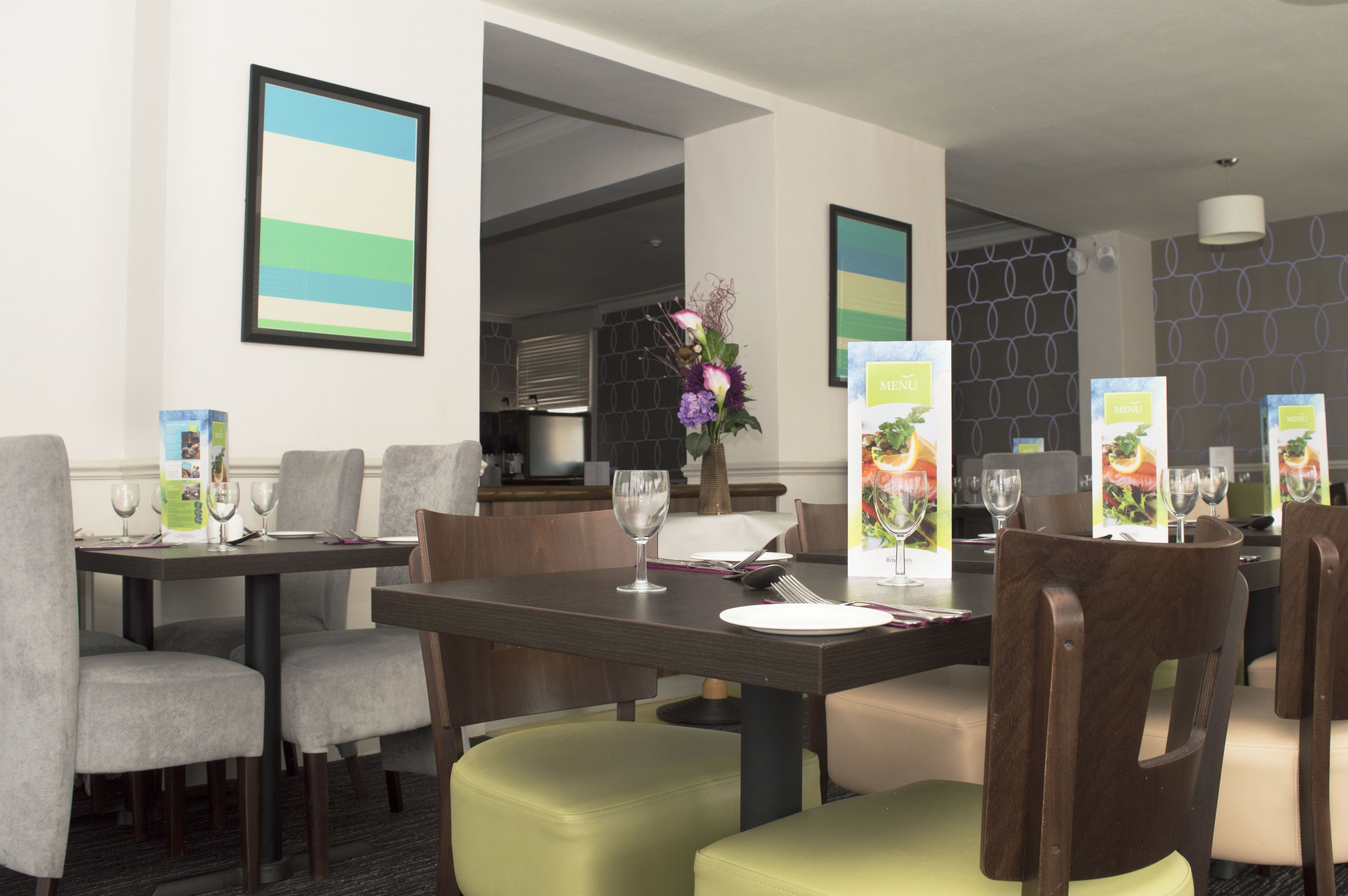 A modern dining area with tables set for four, each with a menu stand, wine glasses, and cutlery.