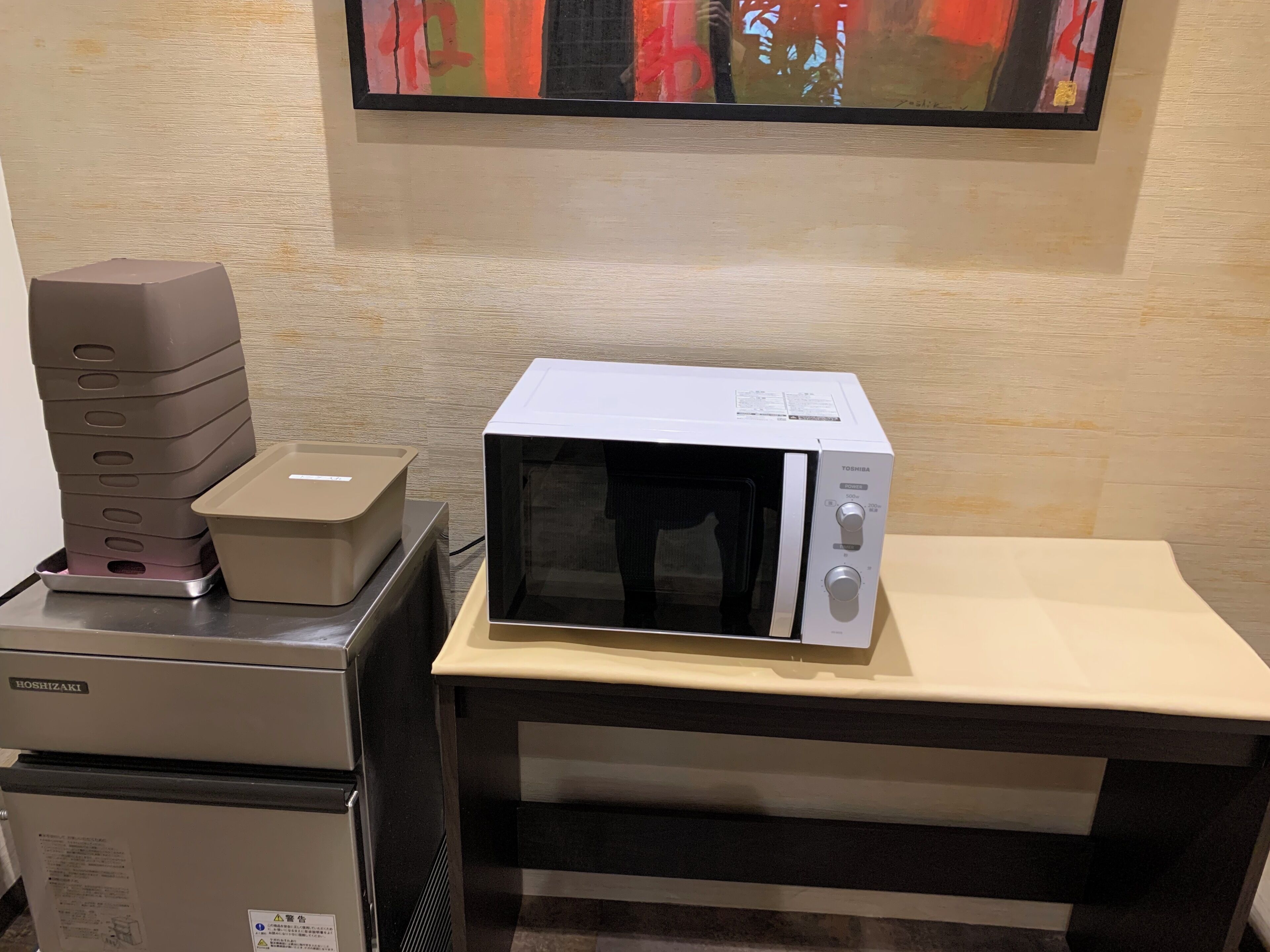 A microwave on a counter with a Toshiba label, a refrigerator, and a stack of plastic containers.