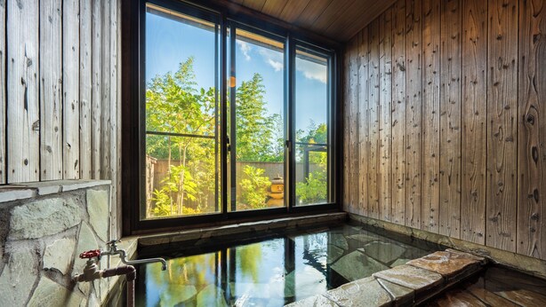 A stone-lined hot tub with a view of a wooden wall and a window overlooking greenery. - Yufuin ZEN - Adults Only (Yufu)