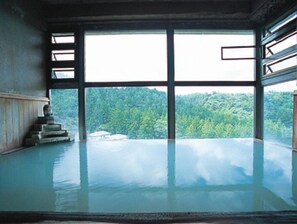 Ein Zimmer mit großem Fenster, einer Steinskulptur und Blick auf einen Wald.