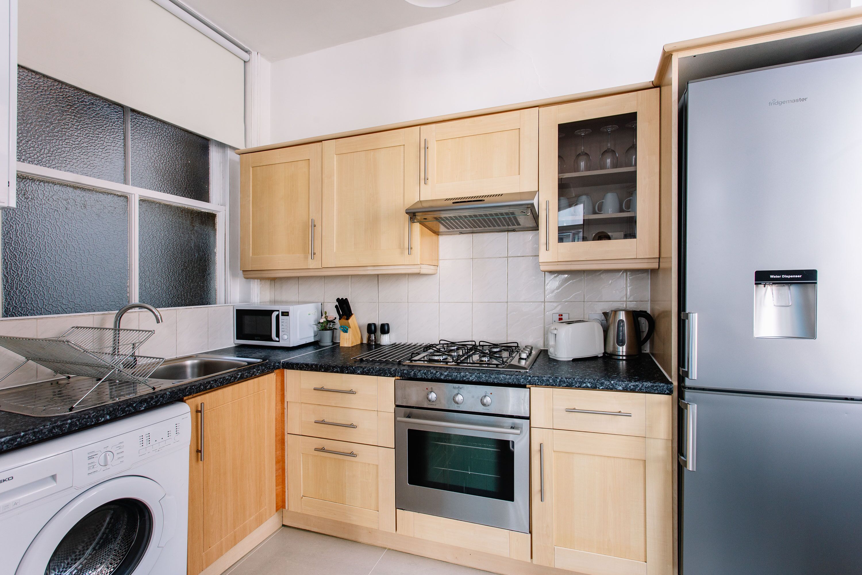 Una cocina moderna con armarios de madera, un refrigerador de acero inoxidable, un horno empotrado y un microondas.