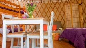 A yurt with a round ceiling, wooden beams, a table with chairs, and a purple bed. - Camping le Beauvillage - Yourte (Lauzerte)