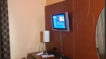 A hotel room with a wooden desk, a computer monitor, a lamp, and a chair.