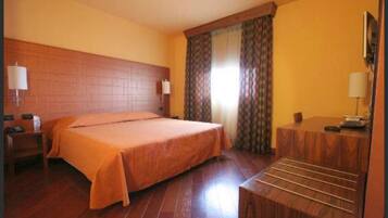 Quarto de hotel com cama grande, cabeceira de madeira, escrivaninha com cadeira e janela com cortinas.