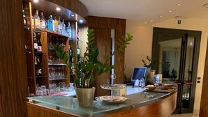 A reception area with a wooden counter, shelves with bottles and glasses, and a potted plant.