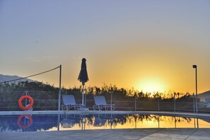 A swimming pool with two lounge chairs and a lifebuoy, reflecting the sunset and mountains in the background. - Reina Apartments (Apokoronas)