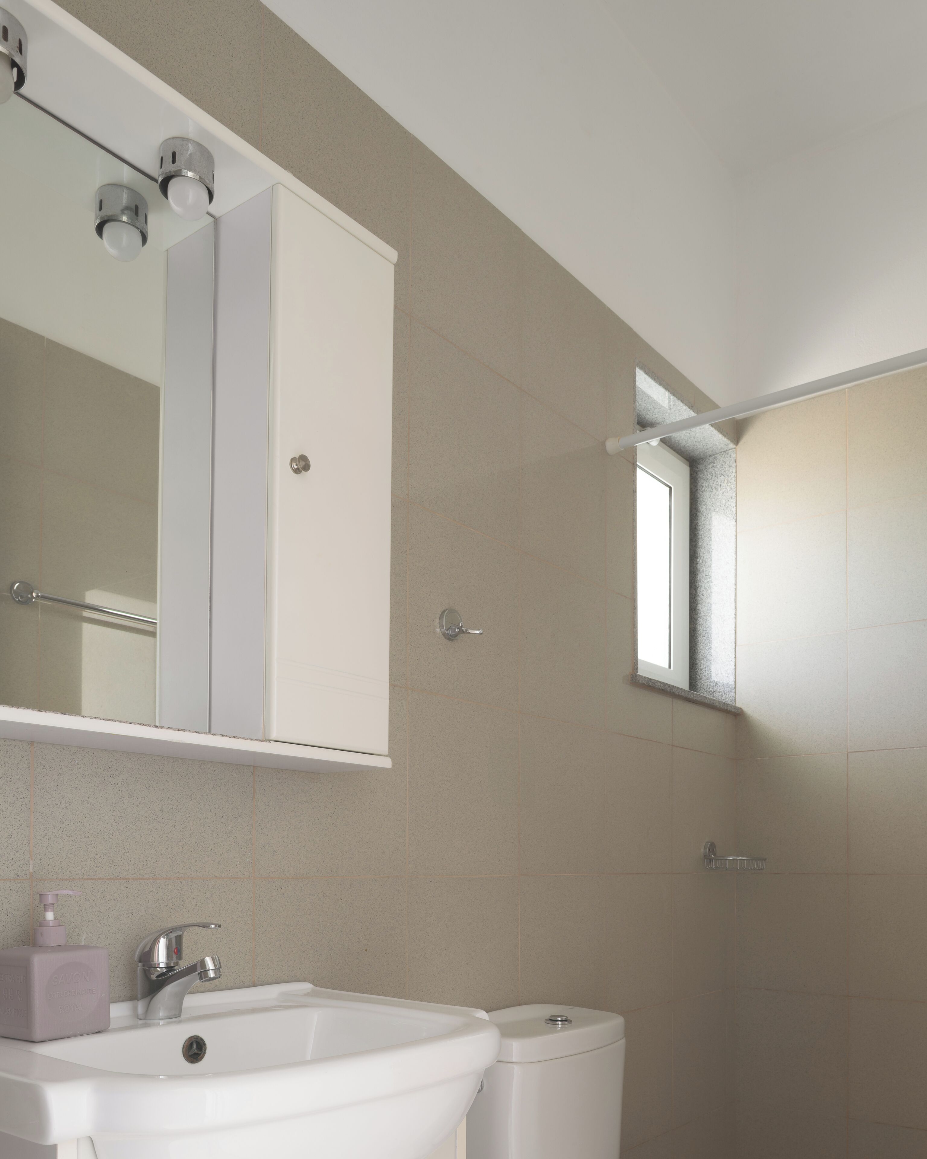 Une salle de bain avec un lavabo blanc, un miroir et une fenêtre.