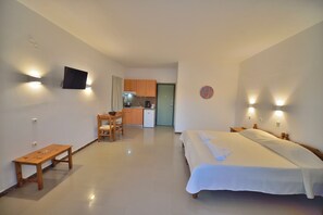 A hotel room with a bed, a small table, a chair, a kitchenette, and a TV mounted on the wall. - Reina Apartments (Apokoronas)