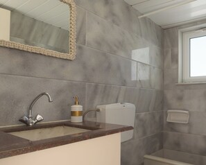 A bathroom with a marble wall, a sink with a faucet, a soap dispenser, and a toilet. - Reina Apartments (Apokoronas)