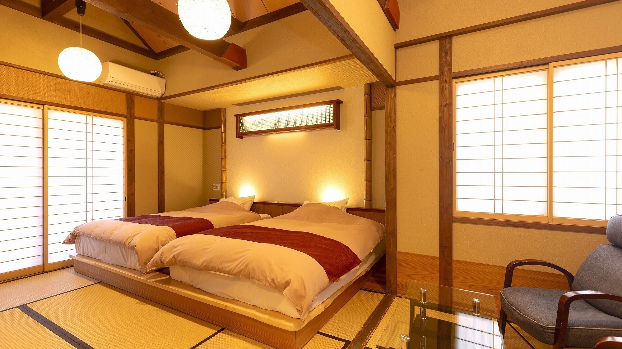 Ein traditioneller japanischer Raum mit Tatami-Böden, einer niedrigen Plattform-Liege, schiebbaren Shoji-Türen und einer Holzzieldecke.