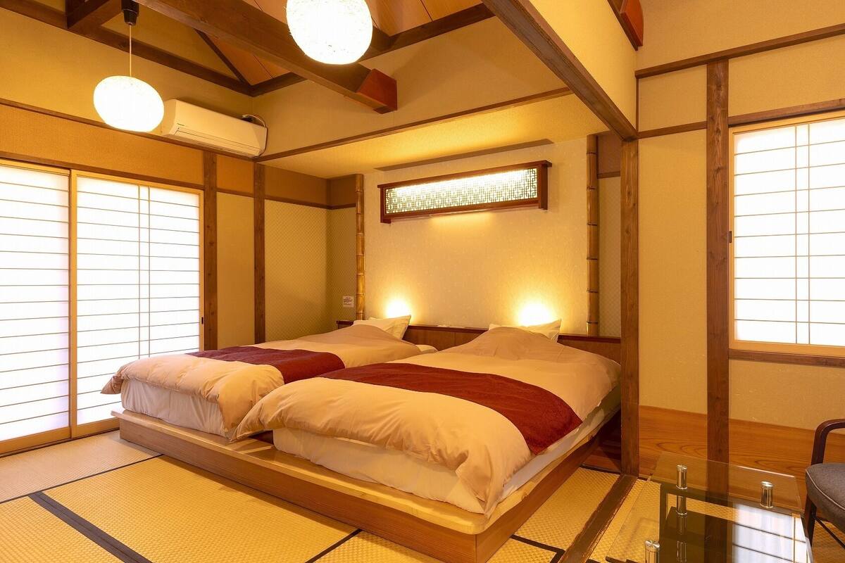 A traditional Japanese-style room with tatami flooring, a low platform bed, sliding shoji doors, and a wooden ceiling.