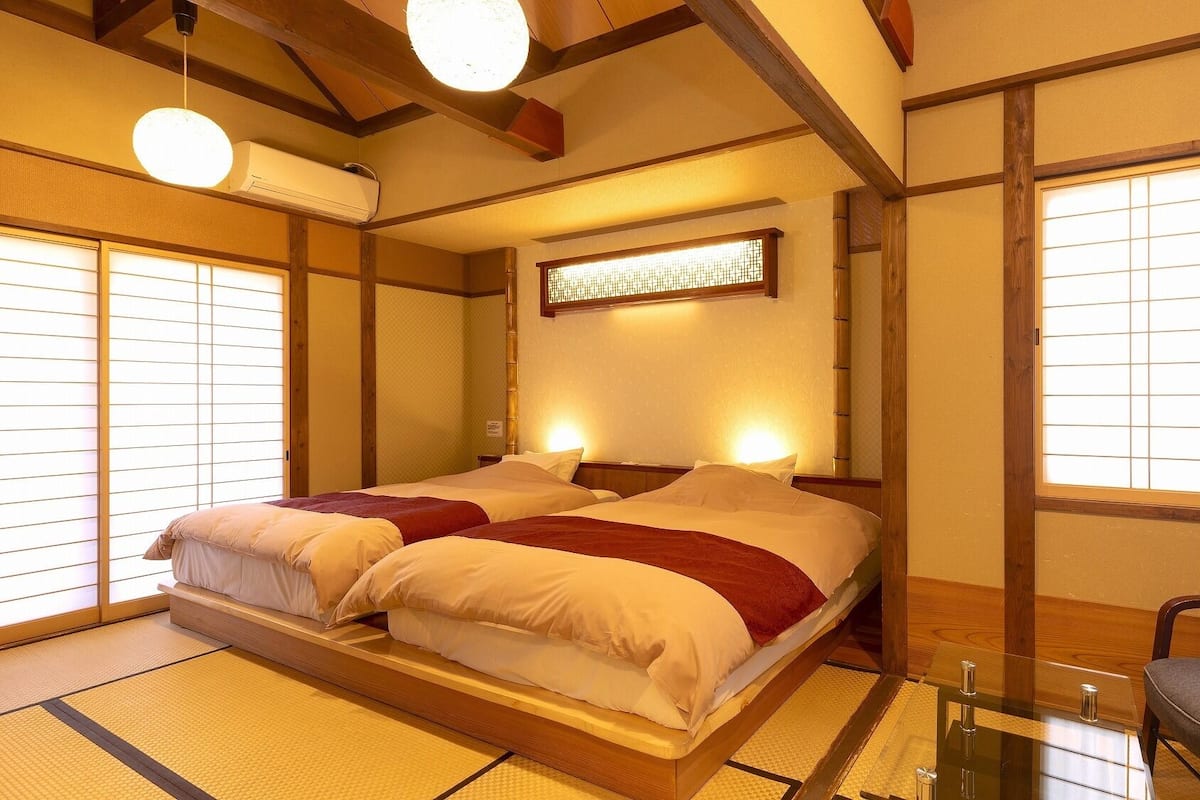 Ein traditioneller japanischer Raum mit Tatami-Böden, einer niedrigen Plattform-Liege, schiebbaren Shoji-Türen und einer Holzzieldecke.