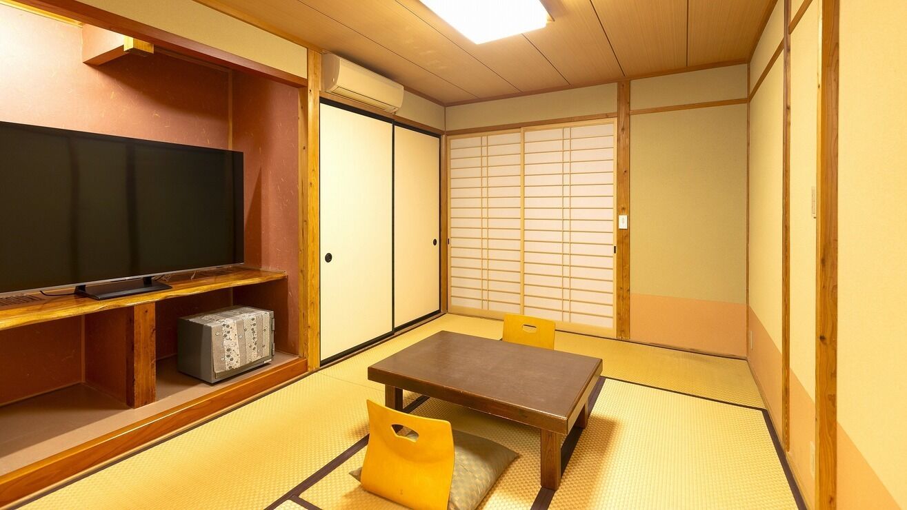 Ein traditioneller japanischer Raum mit Tatami-Böden, einem Fernseher auf einem Holzregal und gleitenden Türen.