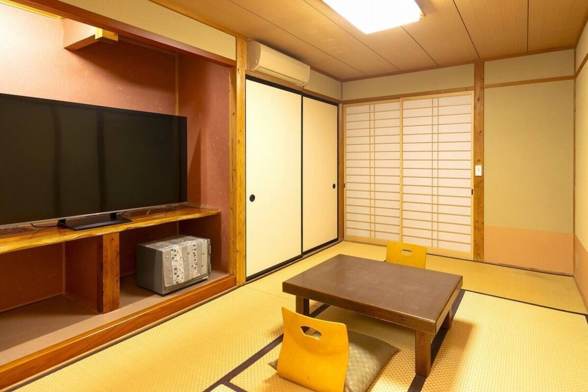A traditional Japanese room with tatami flooring, a television on a wooden shelf, and sliding doors.