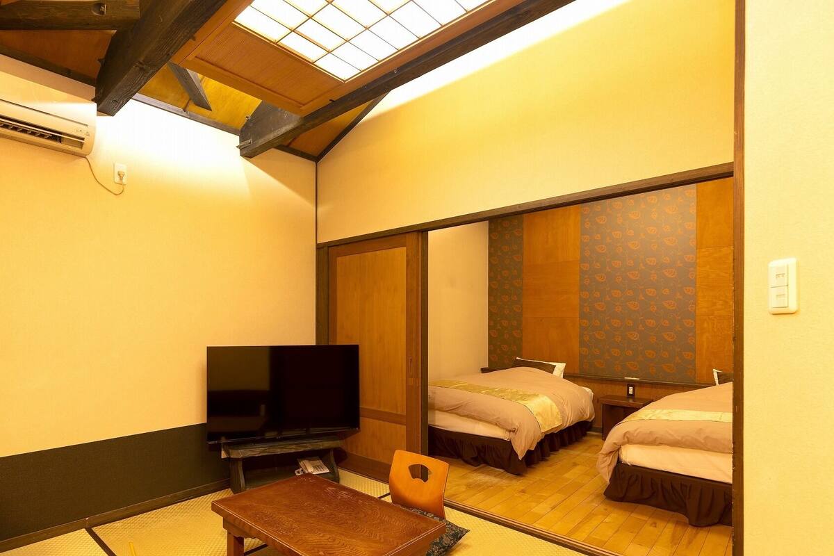 A hotel room with a bed, a television, a small table, and a mirror reflecting the room.