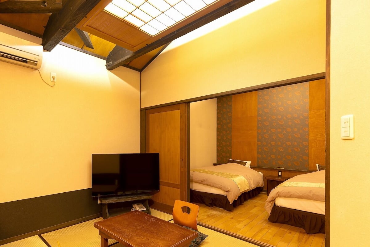 Ein Hotelzimmer mit einem Bett, einem Fernseher, einem kleinen Tisch und einem Spiegel, der das Zimmer widerspiegelt.