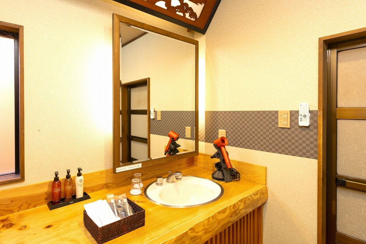 Un baño de hotel con tocador de madera, un espejo grande, un lavamanos y artículos de aseo.