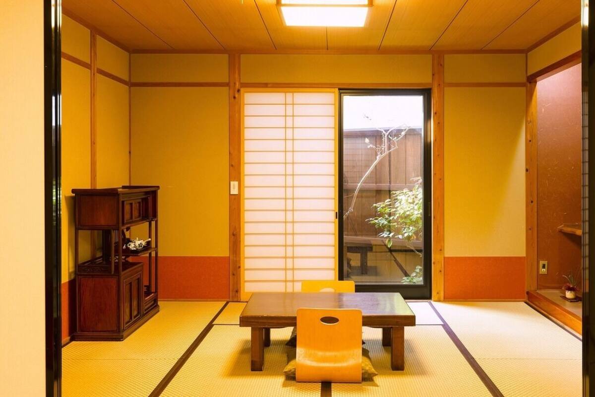 A traditional Japanese room with tatami flooring, a sliding door, a wooden table, and a shelf with decorative items.