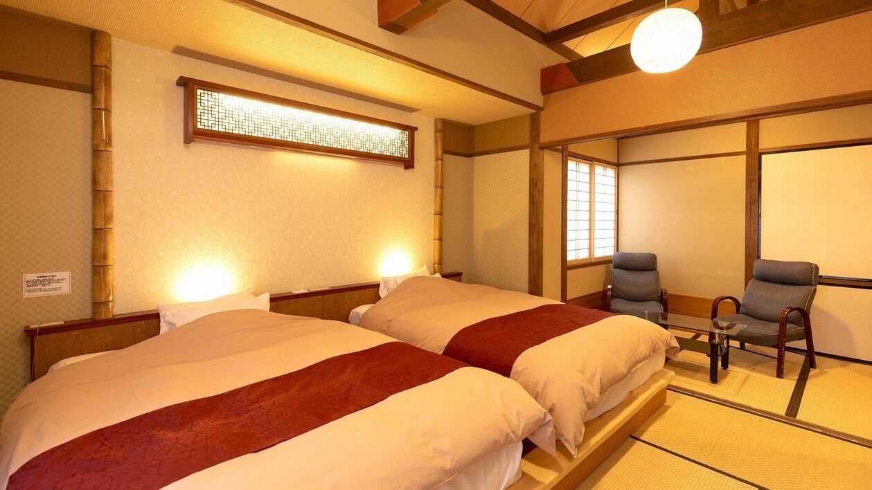 Ein traditionell eingerichtetes Hotelzimmer im japanischen Stil mit zwei Betten, einer Sitzecke und einem Shoji-Bildschirm.