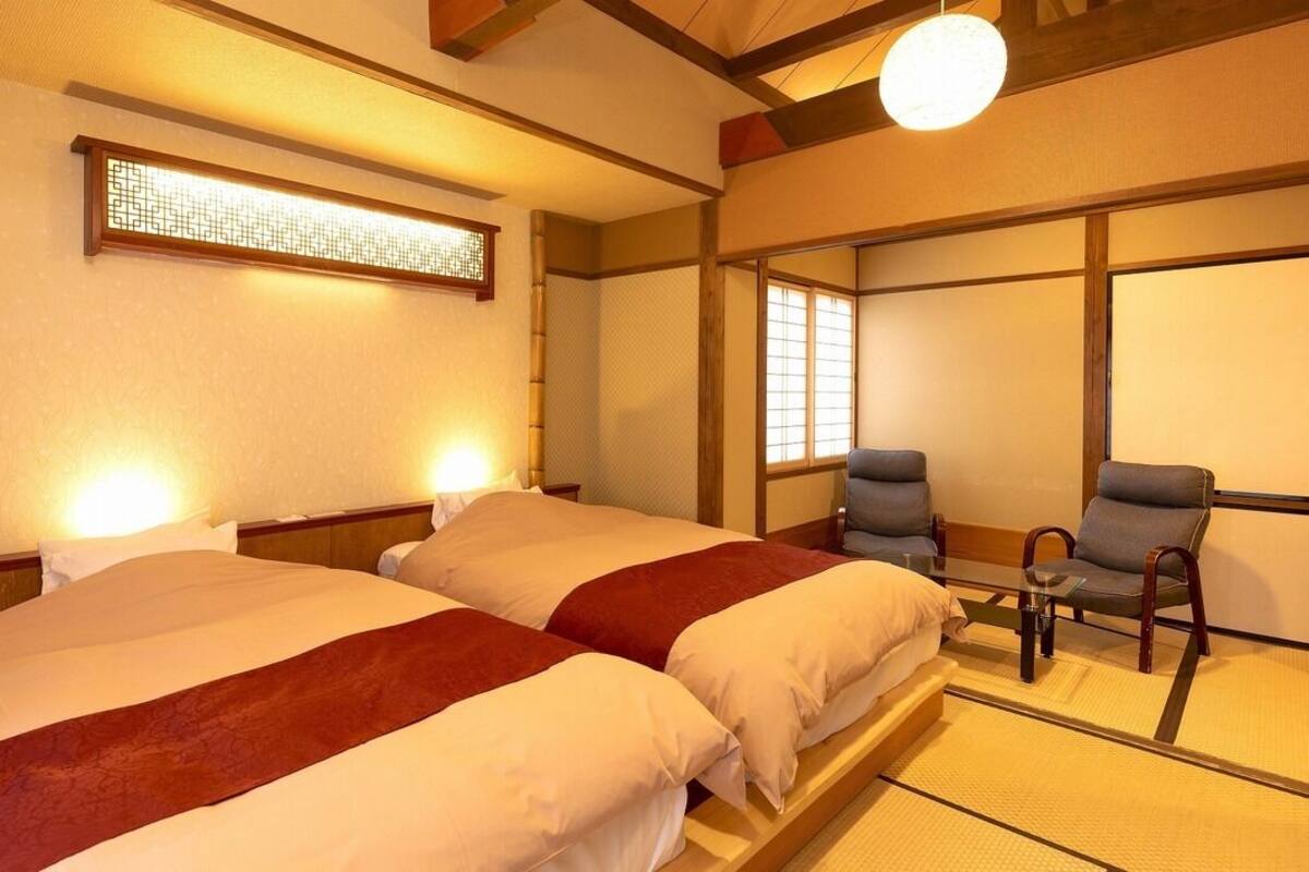 A traditional Japanese-style hotel room with two beds, a sitting area, and a shoji screen.