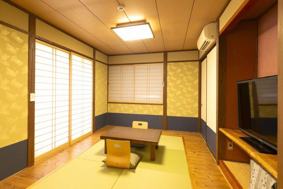 Ein traditioneller japanischer Raum mit Tatami-Böden, einem niedrigen Tisch, einem Stuhl, Schiebetüren aus Shoji-Papier und einem Fernseher.