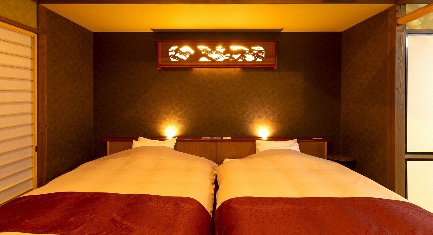 Ein Zimmer mit zwei Betten, einem Holzkopfende und einer an der Wand befestigten Leuchte.