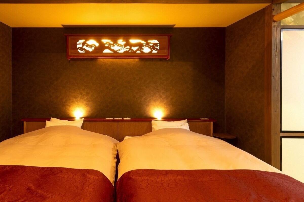 A room with two beds, a wooden headboard, and a wall-mounted light fixture.