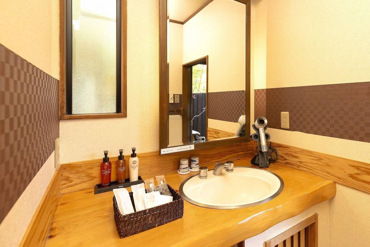 A bathroom with a wooden vanity, a large mirror, a sink, and toiletries.