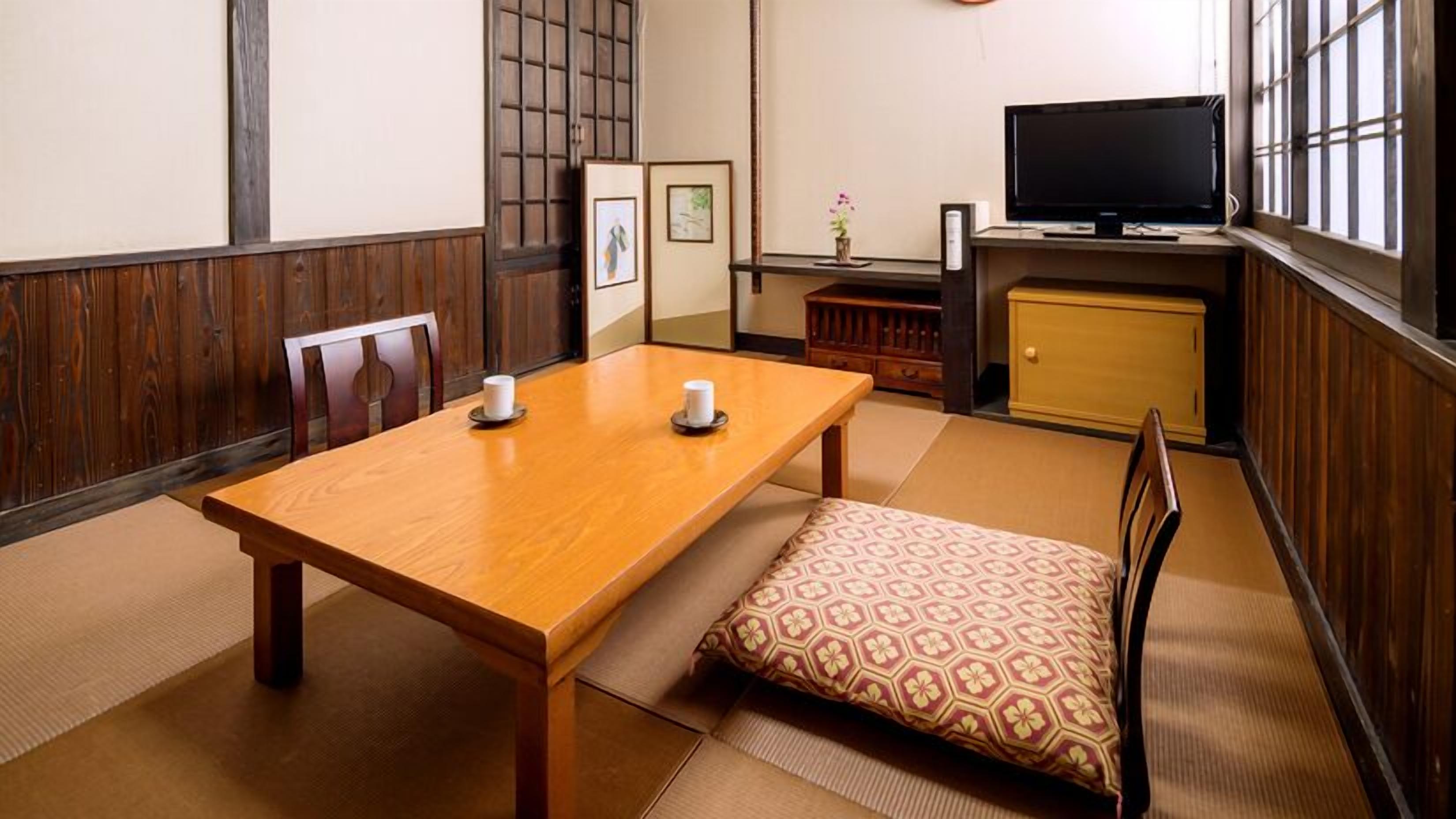 A traditional Japanese room with tatami flooring, a wooden table with two cups, a low wooden cabinet, and a television.