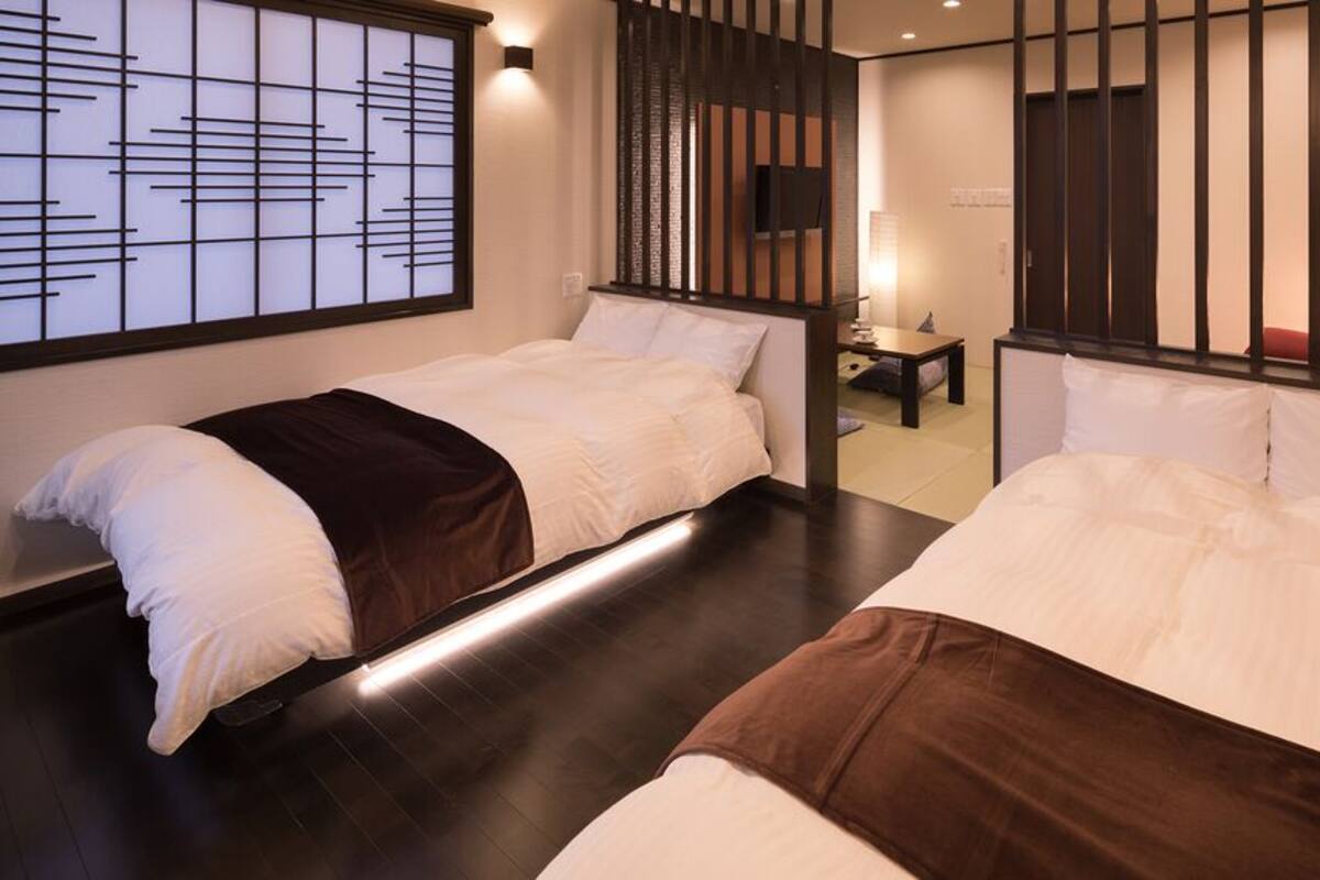 A hotel room with two beds, a TV, a desk, and a sliding door.