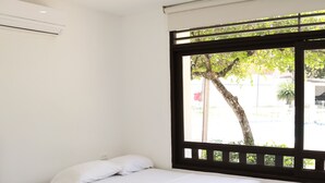 A room with two single beds, a window with a view of greenery, and an air conditioning unit on the wall. - Hotel Restaurante Versalles (Melgar)