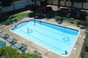 Una piscina rectangular con un borde empedrado, rodeada de sillas de descanso y un pequeño jardín.