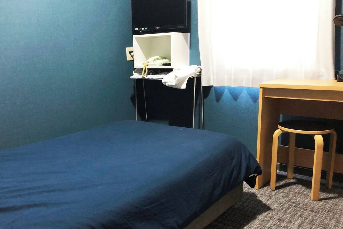 A small, single-bed room with a desk and chair, a television, and a curtain.