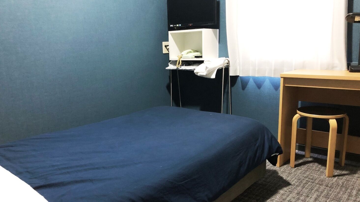Ein kleines Zimmer mit einem Einzelbett, einem Schreibtisch, einem Stuhl, einem Telefon und einem Fernseher auf einem Tisch.