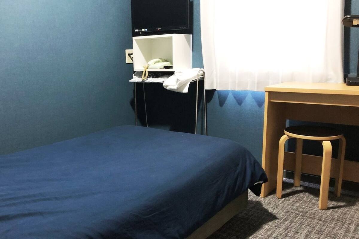 A small, single-bed room with a desk and chair, a telephone, and a television on a stand.