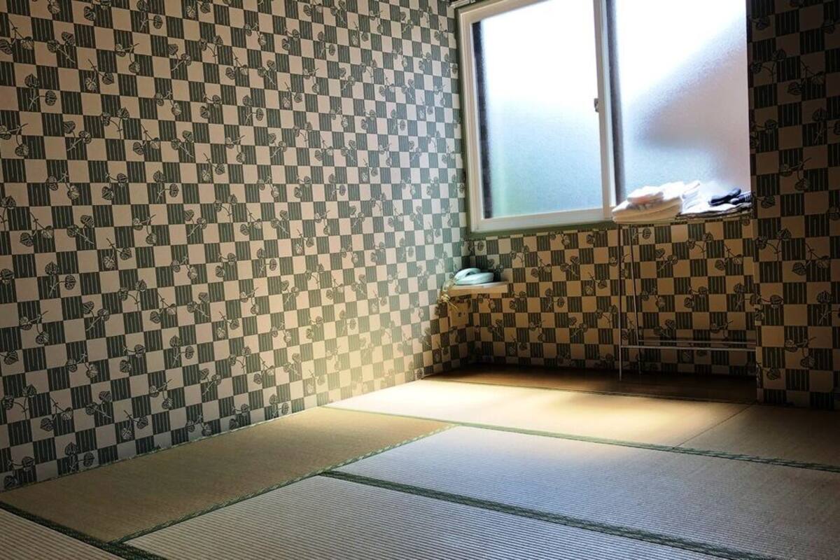 A tatami mat room with a checkered wall pattern, a window, and a small shelf with items.