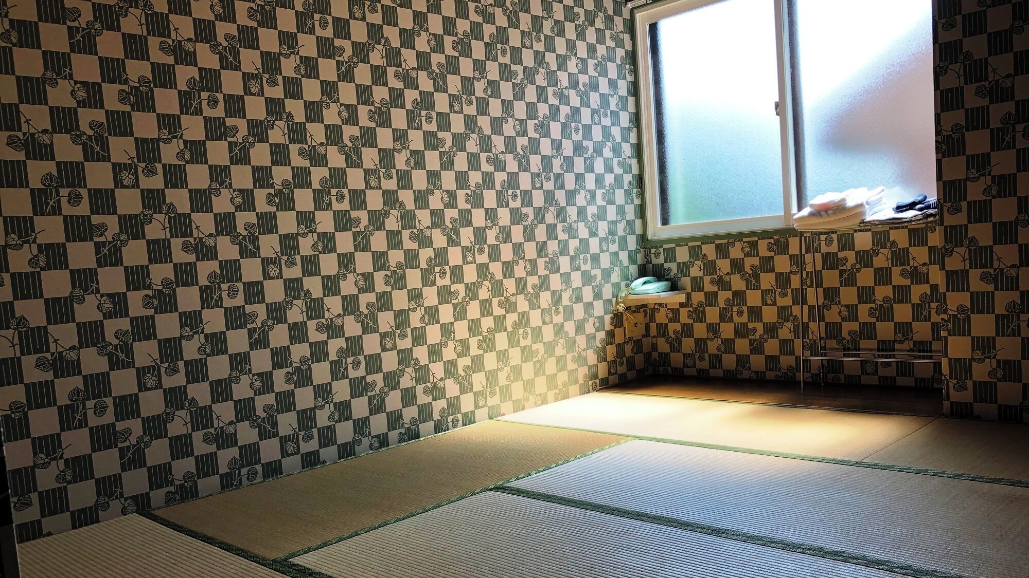 Ein Zimmer mit Tatami-Matten, einem Fenster mit Blick und ornamentalem Wandpapier.