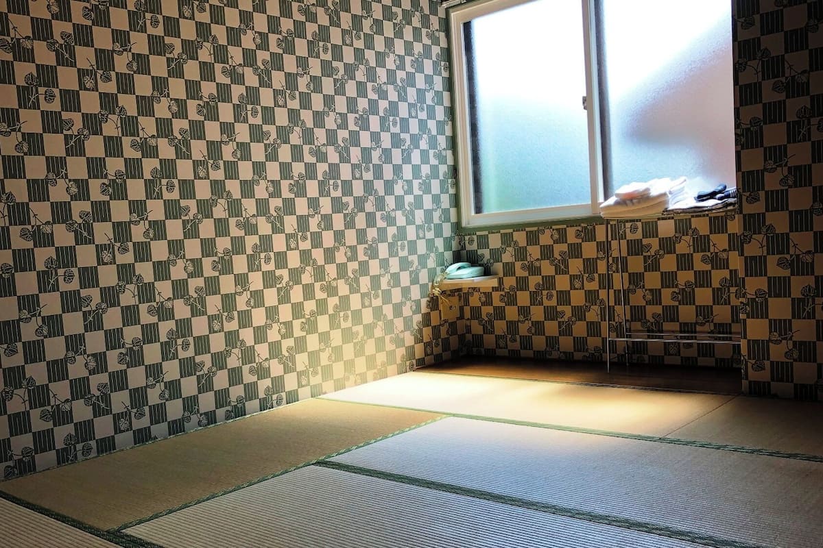 A room with tatami mats, a window with a view, and patterned wallpaper.