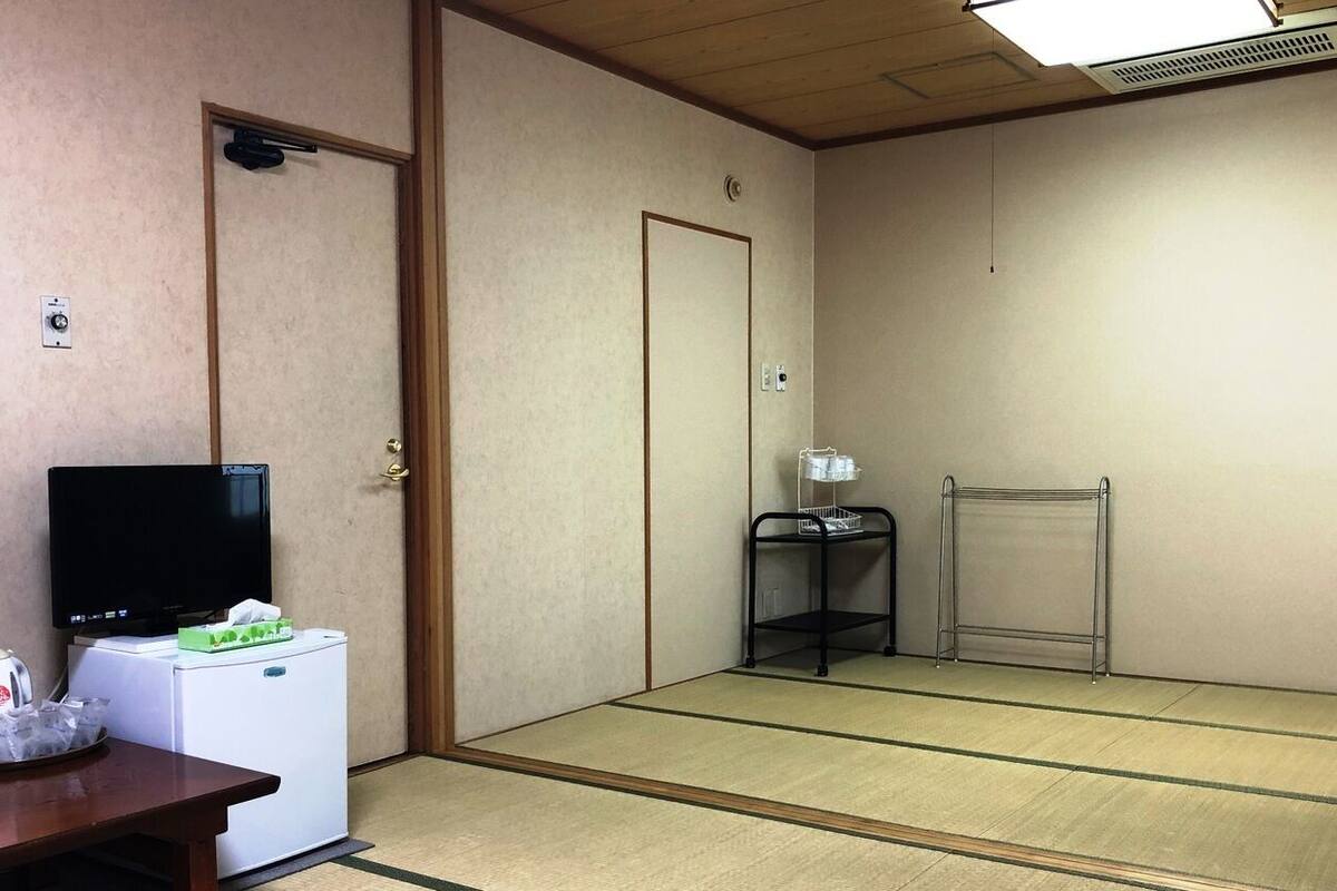 A room with a television, a small refrigerator, a wooden table, a futon bed, and a sliding door.
