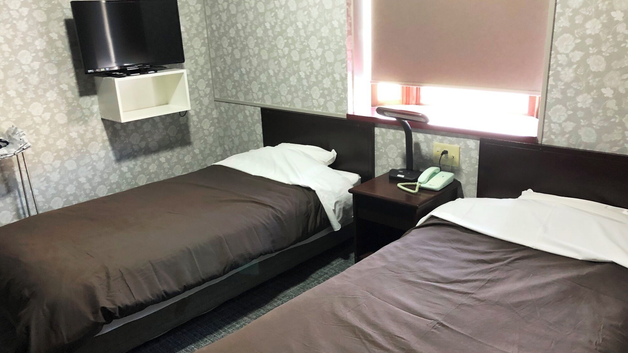 Una camera d'albergo con due letti singoli, un comodino con il telefono e una TV montata a parete.