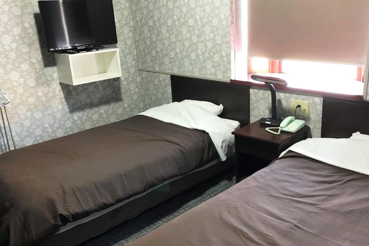 A hotel room with two single beds, a bedside table with a telephone, and a TV mounted on the wall.
