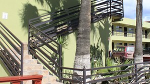 Un escalier avec des rampes en métal, des palmiers et un bâtiment à la façade jaune.