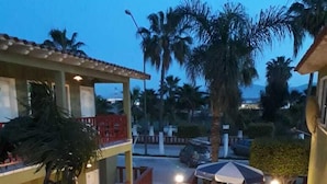 Une cour avec des espaces de détente en plein air, des palmiers et un bâtiment doté d’un toit en tuiles.