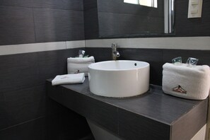 A bathroom with a white sink, dark tiled walls, and a mirror.