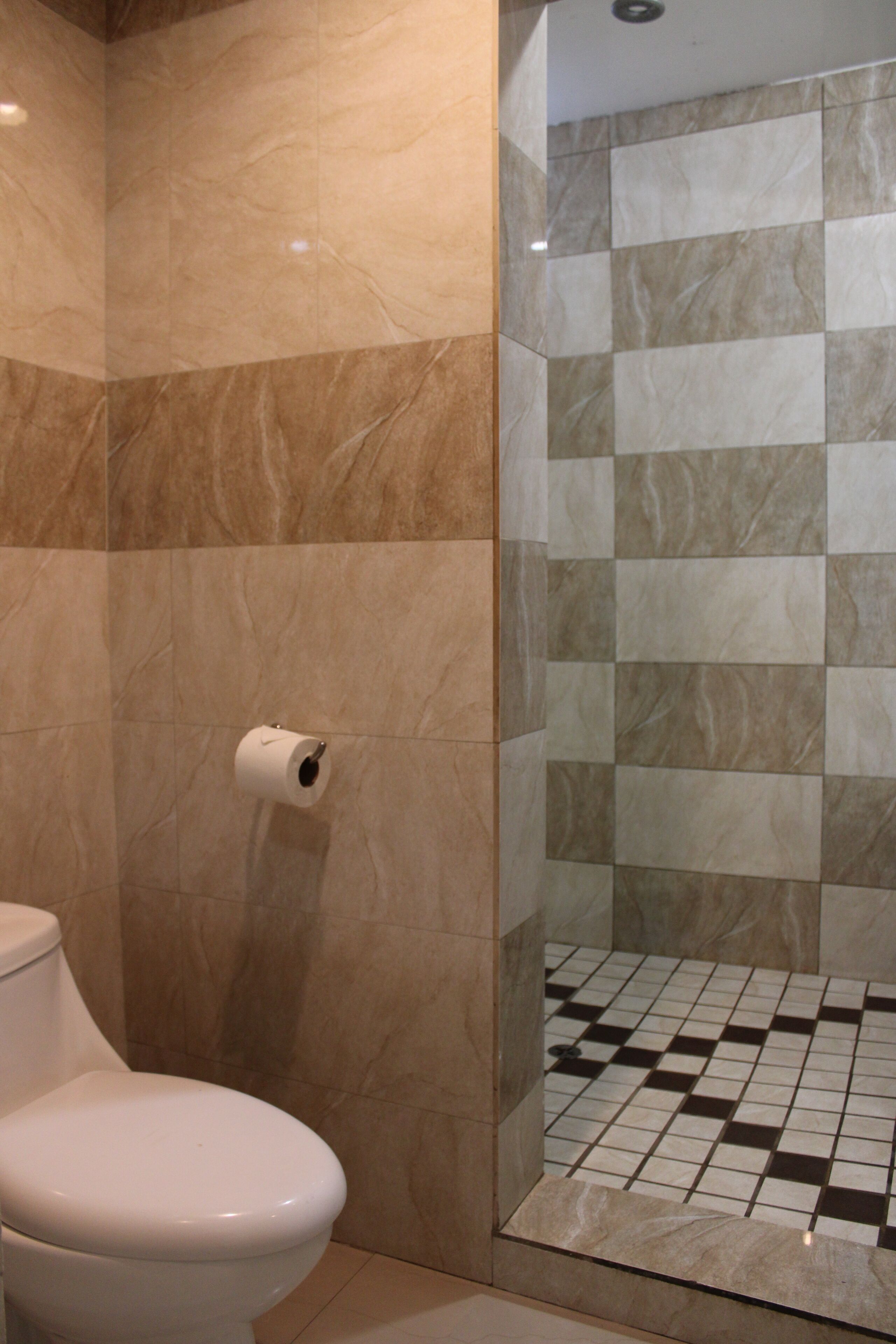 A bathroom with a toilet, a roll of toilet paper, and a shower area with tiled walls and floor.