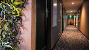 A hallway with a patterned carpet, a plant on the left, and doors on the right. - Personal Hotel You (Takeo)